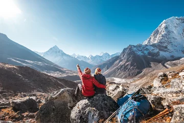 Fototapete Ama Dablam Paar ruht sich auf der Everest Base Camp Trekkingroute in der Nähe von Dughla 4620m aus. Rucksacktouristen verließen Rucksäcke und Trekkingstöcke und genießen den Blick auf das Tal mit dem Gipfel Ama Dablam 6812 m und Tobuche 6495 m