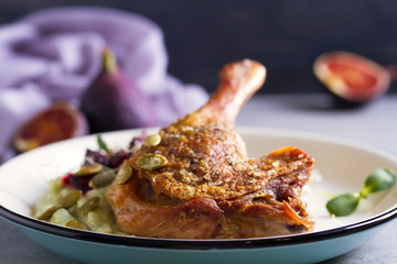 Roast duck leg with mashed green vegetables, beetroot, and pumpkin seeds on light gray background