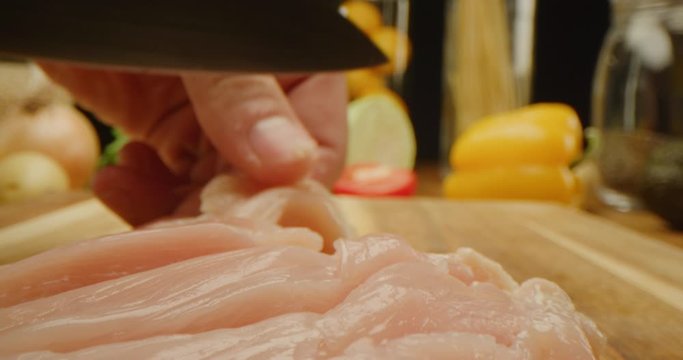 Cutting chicken fillets with chef knife close up, macro shot of cooking process, slow motion, vegetables and kitchen stuff on a table, preparing a dinner, slow motion, red epic