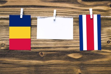 Hanging flags of Chad and Costa Rica attached to rope with clothes pins with copy space on white note paper on wooden background.Diplomatic relations between countries.