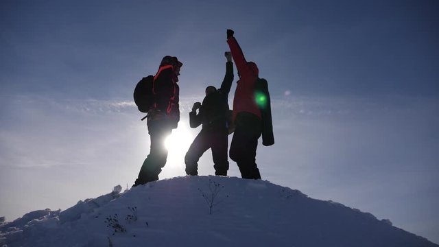Alaskan travelers go to the top of a snowy hill and rejoice in victory against winter sunset. team work of people. business teamwork, victory and success. Tourists met on top of success.