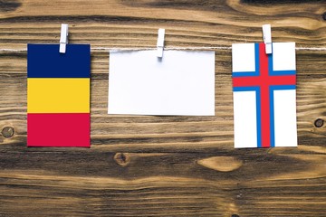 Hanging flags of Chad and Faroe Islands attached to rope with clothes pins with copy space on white note paper on wooden background.Diplomatic relations between countries.