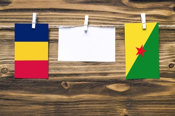 Hanging flags of Chad and French Guiana attached to rope with clothes pins with copy space on white note paper on wooden background.Diplomatic relations between countries.