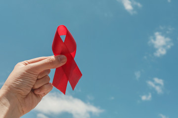hand holding red ribbon over blue sky, hiv awareness concept, world AIDS day, world cancer day