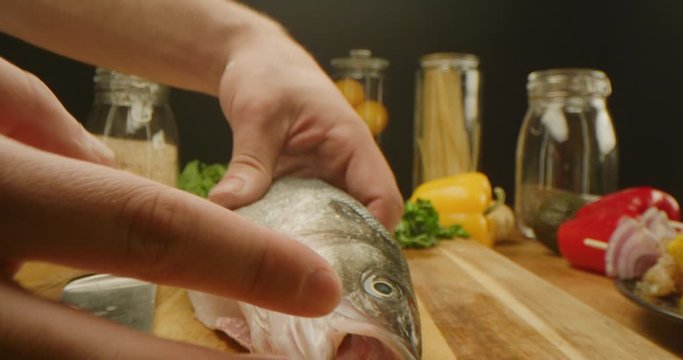 Close up of cutting fish, macro shot of cooking process, vegetables and kitchen stuff on a table, preparing a dinner, slow motion