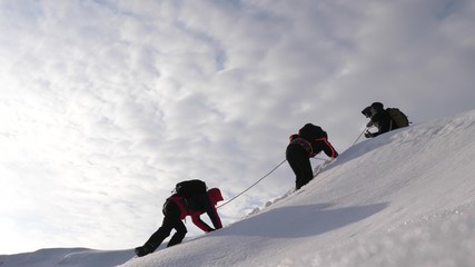 three Alpenists in winter climb rope on mountain. Travelers climb rope to their victory through...
