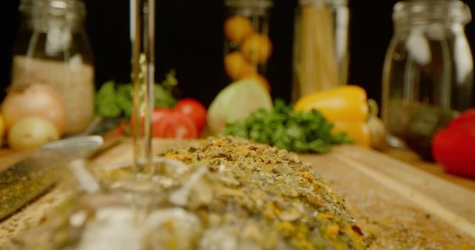 Close up of pouring oil on a seasoned with spices fish, macro shot of cooking process, vegetables and kitchen stuff on a table, preparing a dinner, slow motion