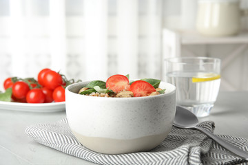 Delicious buckwheat porridge with mushrooms and tomato on table indoors