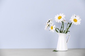 Beautiful tender chamomile flowers in jug on table against light background, space for text