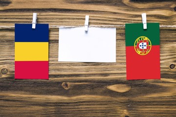 Hanging flags of Chad and Portugal attached to rope with clothes pins with copy space on white note paper on wooden background.Diplomatic relations between countries.