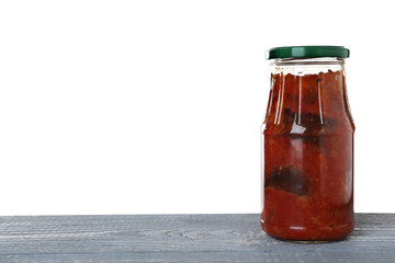 Jar of vegetable sauce on blue wooden table against white background. Pickled food