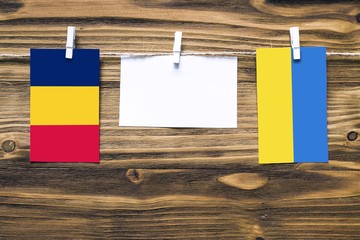 Hanging flags of Chad and Ukraine attached to rope with clothes pins with copy space on white note paper on wooden background.Diplomatic relations between countries.