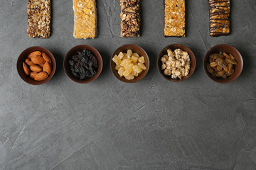 Healthy granola bars and bowls with ingredients on grey table, flat lay. Space for text