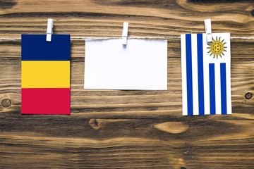 Hanging flags of Chad and Uruguay attached to rope with clothes pins with copy space on white note paper on wooden background.Diplomatic relations between countries.