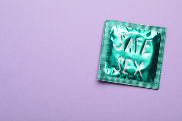 Green condom with phrase SAFE SEX on violet background, top view with space for text