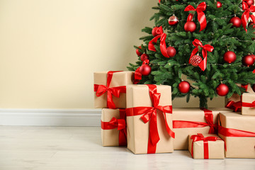 Decorated Christmas tree and gift boxes near beige wall. Space for text