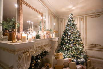 Christmas evening in the light of candles and garlands. Classic luxurious apartments with decorated christmas tree and presents. Living with fireplace, columns and stucco.