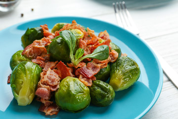 Tasty roasted Brussels sprouts with bacon on white wooden table, closeup