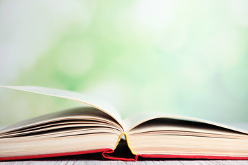 Open book on white wooden table against blurred green background, closeup. Space for text