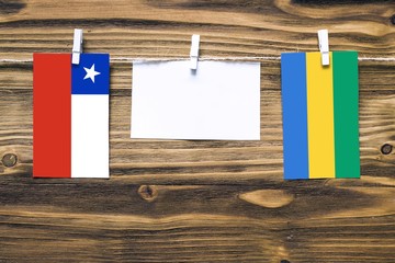 Hanging flags of Chile and Gabon attached to rope with clothes pins with copy space on white note paper on wooden background.Diplomatic relations between countries.