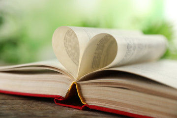 Heart made of book pages on wooden table against blurred background, closeup