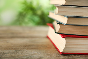 Stack of hardcover books on wooden table against blurred background, closeup. Space for text