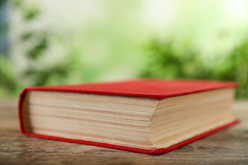 Closed hardcover book on wooden table against blurred background
