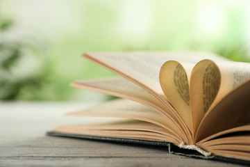 Heart made of book pages on wooden table against blurred background, closeup