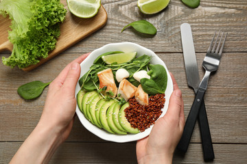 Woman holding bowl of delicious avocado salad with chicken at wooden table, top view