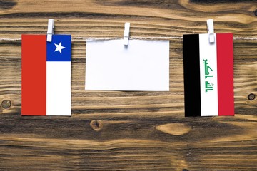 Hanging flags of Chile and Iraq attached to rope with clothes pins with copy space on white note paper on wooden background.Diplomatic relations between countries.