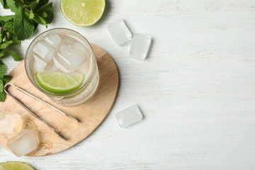 Flat lay composition of cocktail with vodka, ice and lime on white wooden table. Space for text