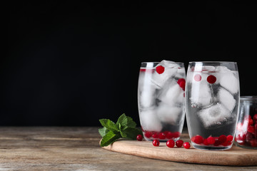 Glasses of cocktail with vodka, ice and cranberry on wooden table against black background. Space...