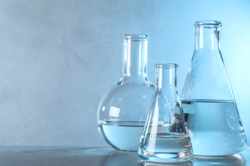 Laboratory glassware with liquid samples for analysis on table against toned blue background, space for text