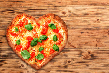 Delicious heart-shapped pizza on wooden background