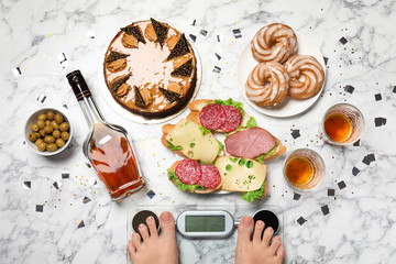Woman using scale surrounded by food and alcohol after party on floor, top view. Overweight problem