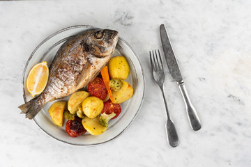 Baked dorado (dorada) fish on a plate, top view