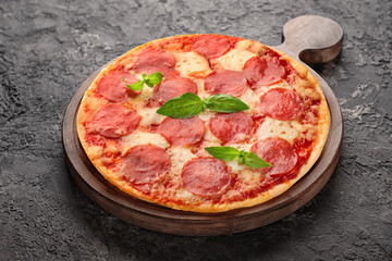 Wooden board with tasty pizza on dark grey background