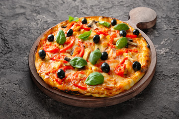 Wooden board with tasty pizza on dark grey background