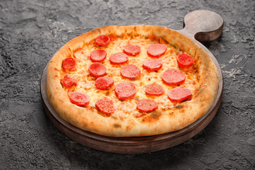 Wooden board with tasty pizza on dark grey background