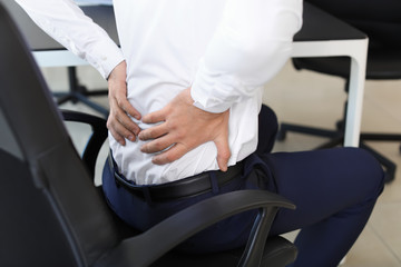 Young man suffering from back pain in office