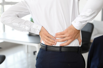 Young man suffering from back pain in office