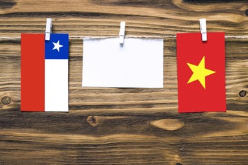 Hanging flags of Chile and Vietnam attached to rope with clothes pins with copy space on white note paper on wooden background.Diplomatic relations between countries.