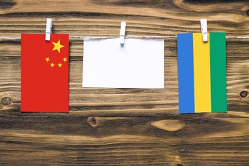 Hanging flags of China and Gabon attached to rope with clothes pins with copy space on white note paper on wooden background.Diplomatic relations between countries.