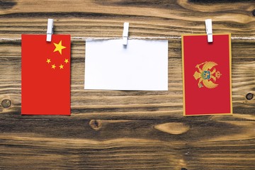 Hanging flags of China and Montenegro attached to rope with clothes pins with copy space on white note paper on wooden background.Diplomatic relations between countries.