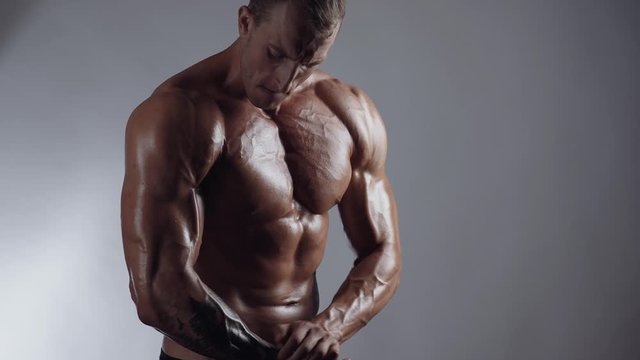 Handsome shirtless athletic man posing on a gray background. Athletic bodybuilder posing