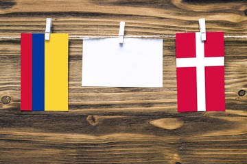 Hanging flags of Colombia and Denmark attached to rope with clothes pins with copy space on white note paper on wooden background.Diplomatic relations between countries.