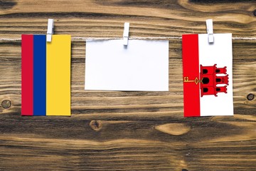 Hanging flags of Colombia and Gibraltar attached to rope with clothes pins with copy space on white note paper on wooden background.Diplomatic relations between countries.