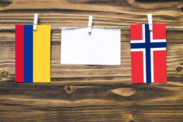 Hanging flags of Colombia and Norway attached to rope with clothes pins with copy space on white note paper on wooden background.Diplomatic relations between countries.