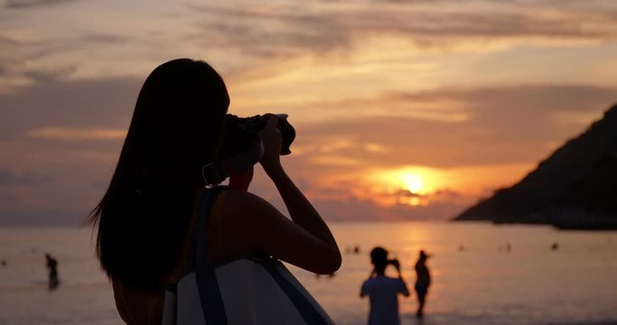 Woman take photo on camera at the sea beach under beautiful sunset