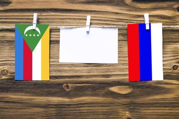 Hanging flags of Comoros and Russia attached to rope with clothes pins with copy space on white...